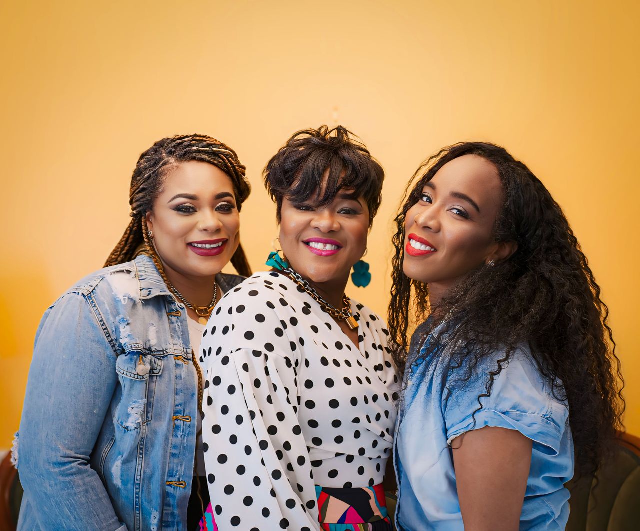 Three women smiling joyfully against a vibrant yellow background.