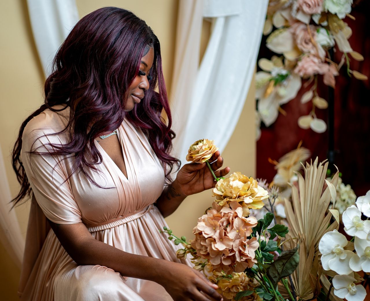 Elegant portrait of a woman in a soft dress arranging flowers indoors.