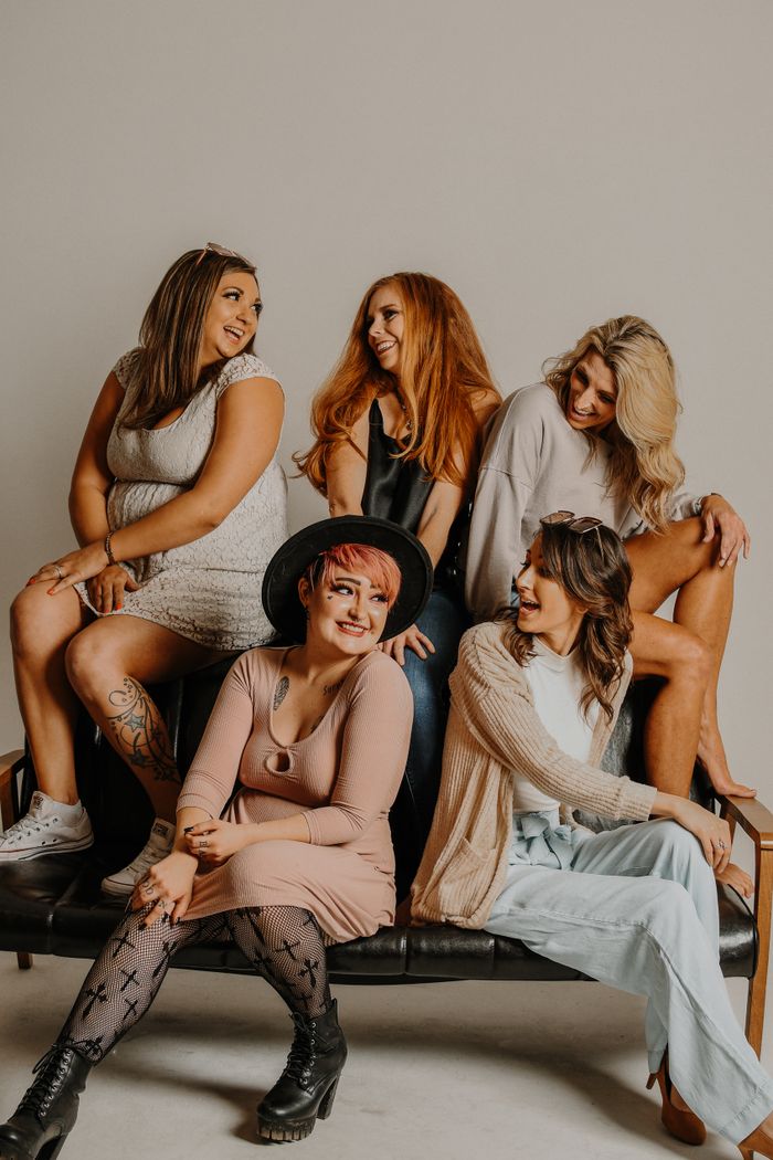 Group of cheerful models with different body types hairstyles and outfits sitting on couch in studio against gray background